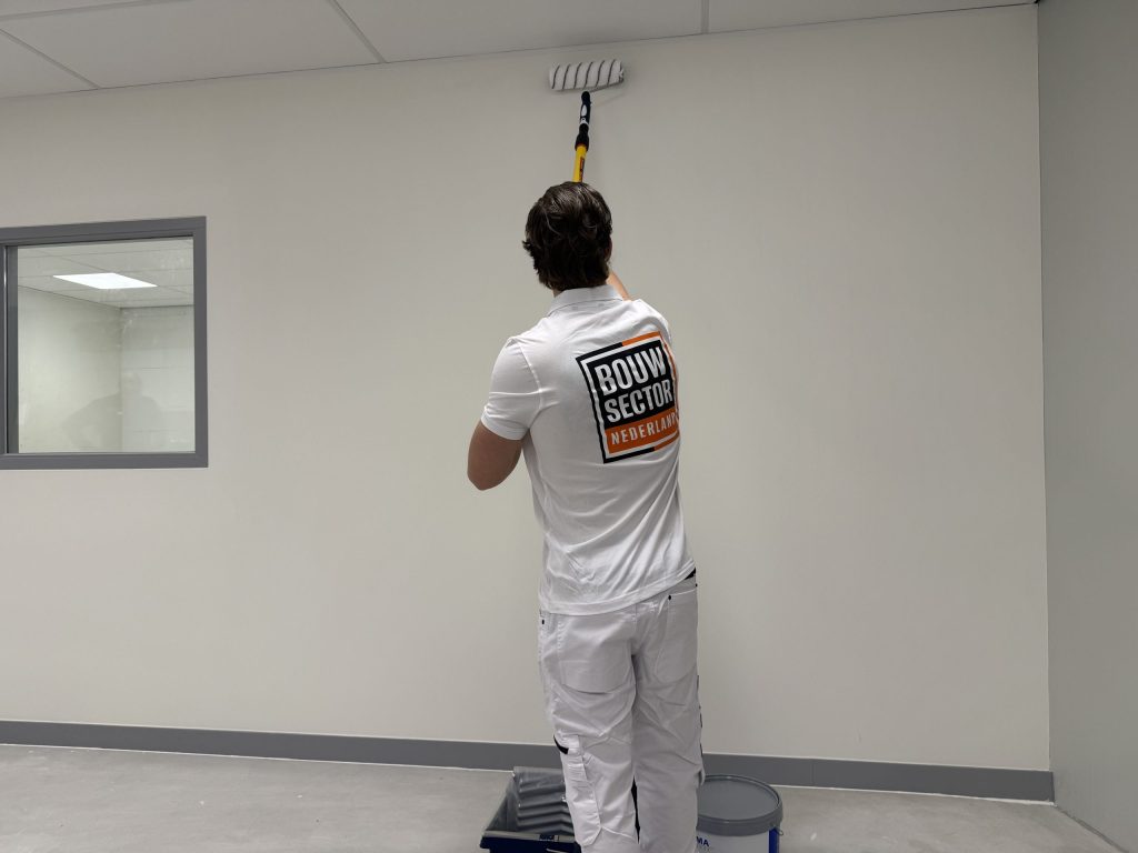 Schilder in witte werkkleding rolt een lichte muur tot tegen het plafond