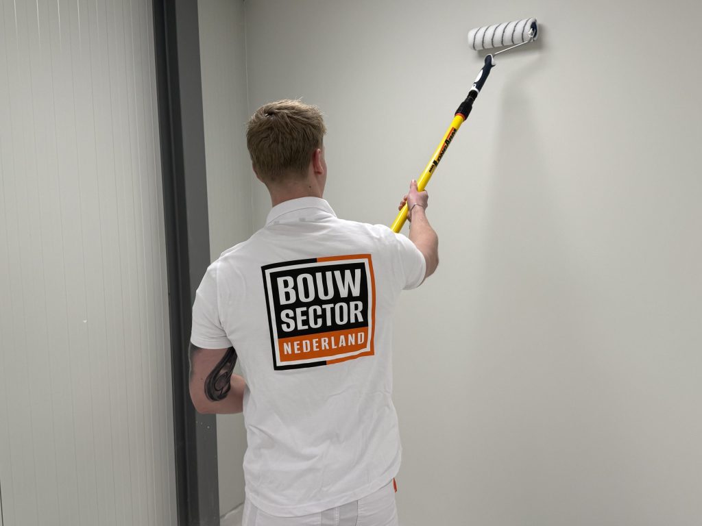 Schilder rolt een witte binnenmuur met een roller aan een verlengsteel