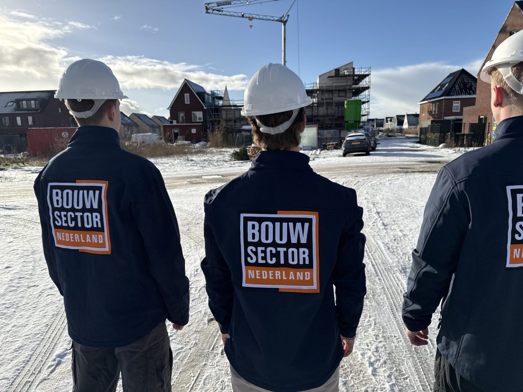 Drie vakmensen van Bouwsector Nederland met witte helm kijken uit over een straat met nieuwe woningen