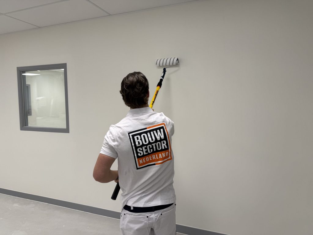 Schilder van Bouwsector Nederland rolt een lichte wand naast een binnenraam