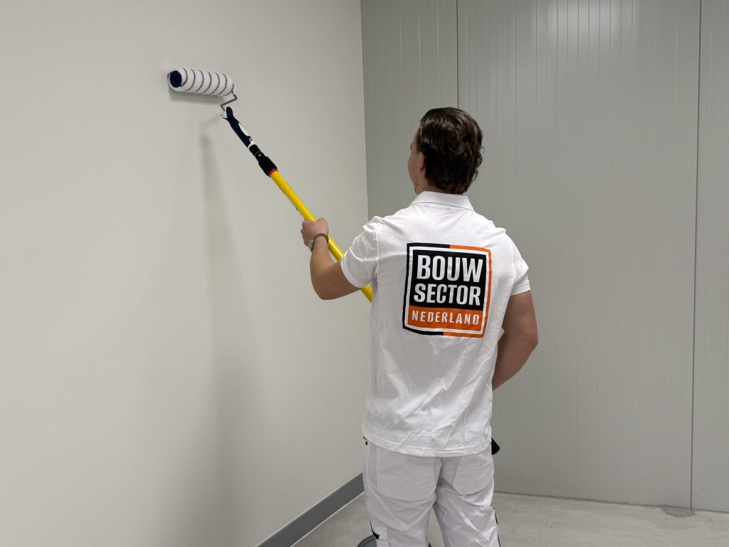 Schilder van Bouwsector Nederland rolt een lege witte wand met een roller aan een gele steel