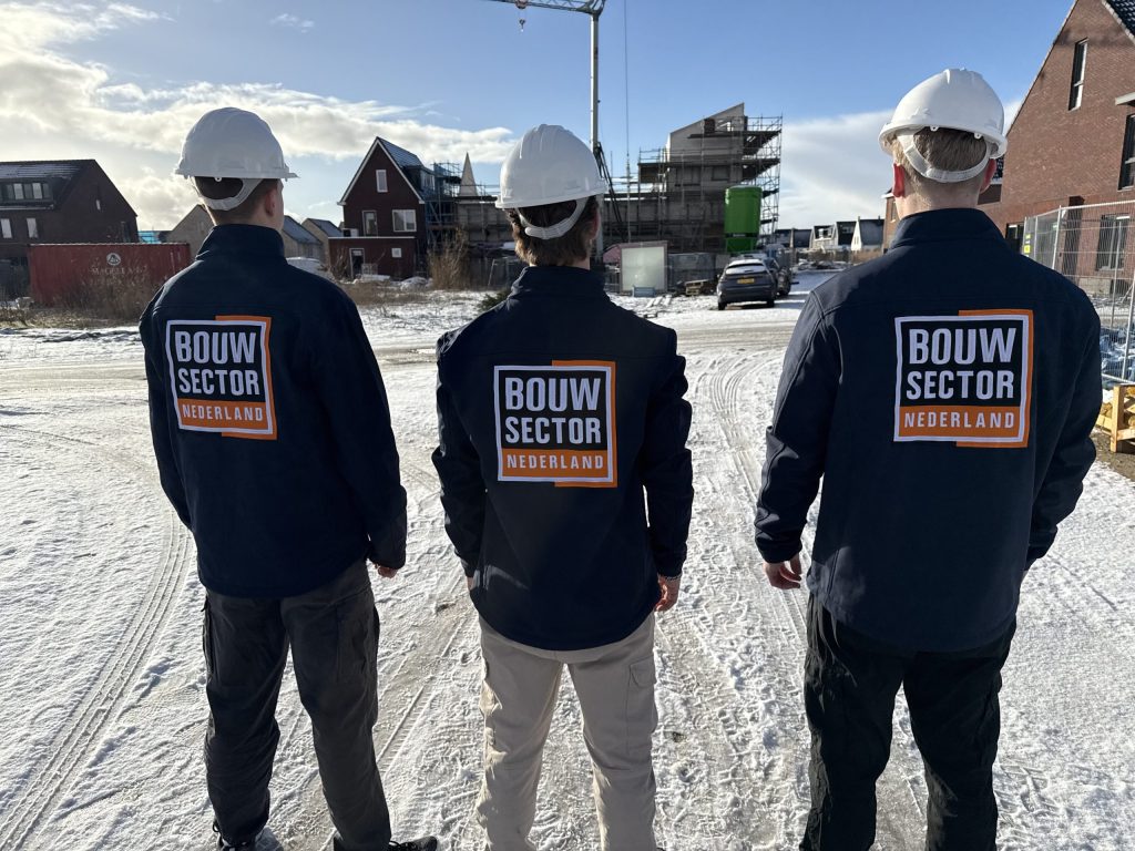 Drie vakmensen van Bouwsector Nederland met witte helm kijken naar woningen in aanbouw met een bouwkraan